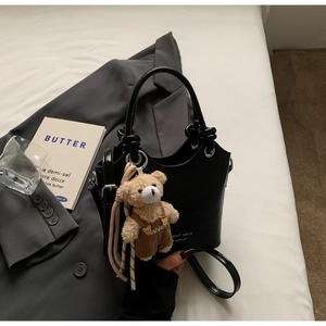 Detail of black crocodile texture handbag with a cute teddy bear plush accessory charm