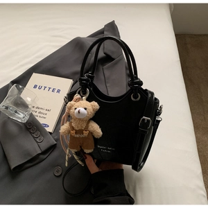 Detail of black embossed leather handbag with cute plush bear charm and adjustable strap