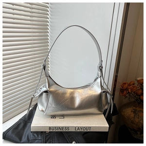 Détail d'un sac hobo argenté métallisé plissé avec pompons sur un livre blanc