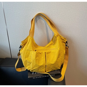 Detail of yellow nylon tote bag featuring front zipper pocket and adjustable shoulder strap