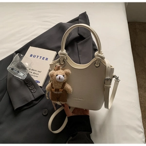 Detail view of cream white faux crocodile leather bucket bag with cute plush bear charm