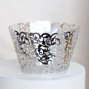 Close-up of laser-cut silver cupcake wrappers with intricate vine and leaf filigree pattern