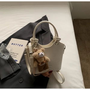 Close-up of off-white crocodile pattern bucket bag with cute bear plush charm and strap