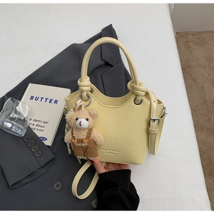 Detail of pale yellow crocodile texture handbag with cute teddy bear charm and logo
