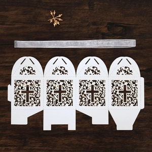 Flat lay of white laser-cut wedding favor box with cross pattern and silver ribbon
