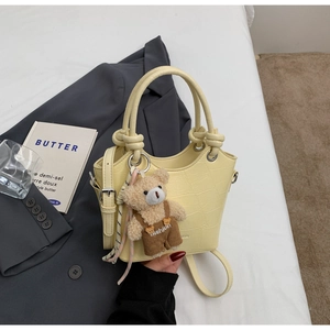 Detail of yellow crocodile pattern bucket bag with cute bear charm and thin shoulder strap