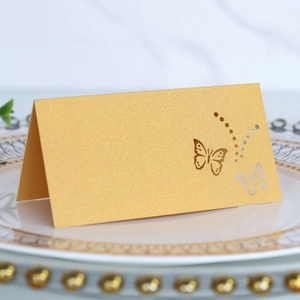 Detail of gold pearlescent table place card featuring laser-cut butterfly design on a plate