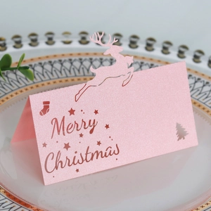 Nahaufnahme der rosa Platzkarte aus Perlmuttpapier mit gelasertem Rentier und Weihnachtsbaum