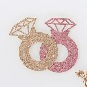 Detail of glitter champagne and pink diamond ring place cards on white surface