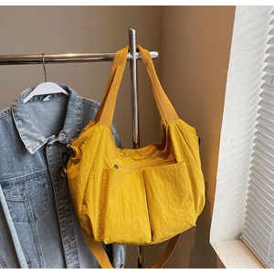Detail of a large yellow nylon tote bag featuring dual front pockets and adjustable strap