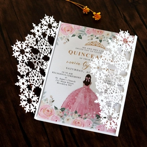 Detail of laser-cut snowflake invitation with pink floral gown theme on wood background