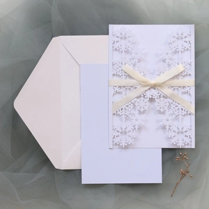 Macro shot of white laser-cut snowflake invitation with ivory ribbon on tulle background