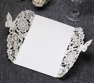 Detail of laser-cut white wedding invitation featuring intricate butterfly and flower patterns