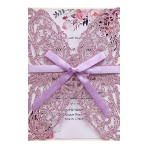 Detail view of laser-cut glitter butterfly wedding invitation with a satin ribbon bow