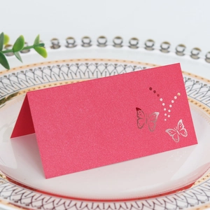 Laser-cut red pearlescent wedding place card with a butterfly design on a ceramic plate