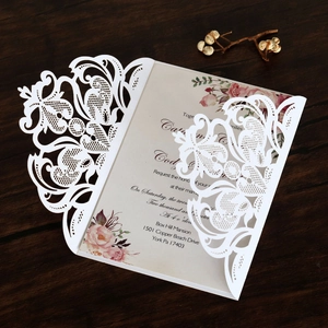 Detailed laser-cut lace wedding invitation with delicate floral insert on wood background