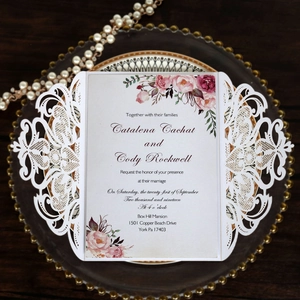 Detailed laser-cut wedding invitation with soft pink roses on a decorative glass tray