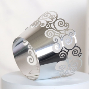 Close-up of laser-cut silver metallic cupcake wrapper with intricate cloud patterns