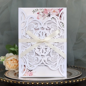 Detailed laser-cut white wedding invitation with elegant cream ribbon on a gold-rimmed plate