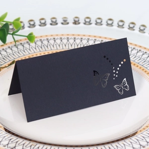 Detail of laser-cut black butterfly place card standing on a white plate for weddings