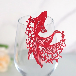 Detail of red laser-cut goldfish paper place card on wine glass rim for wedding decor