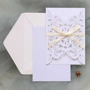 Detail of laser-cut floral wedding invitation with silk bow and white envelope