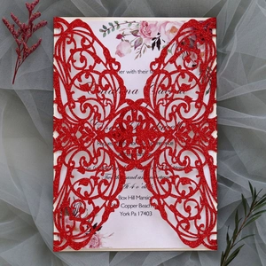 Close-up of red glitter laser-cut invitation with floral inner card on grey tulle