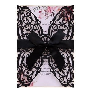 Close-up of black glitter laser-cut lace invitation with a satin bow and floral inner card