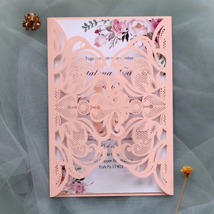 Close-up of laser-cut lace pattern on light pink wedding invitation with floral insert