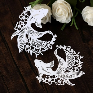 Close-up of white laser-cut goldfish paper place cards on a dark wooden background