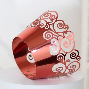 Detail of rose gold laser-cut cupcake wrapper with intricate mirror-finish scroll patterns
