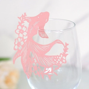 Detail of pink laser-cut goldfish paper card on a glass rim for party decoration