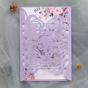 Detail of laser-cut purple lace wedding invitation with floral inner card on gray mesh background
