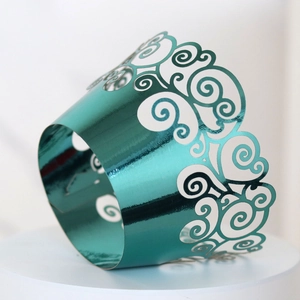 Macro detail of laser-cut teal cupcake wrapper with elegant metallic scrollwork pattern