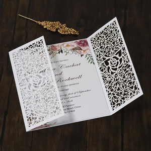 Detail of laser-cut white rose wedding invitation on a rustic dark wood background