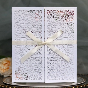 Elegant white laser-cut wedding invitation with cream ribbon on a vintage plate