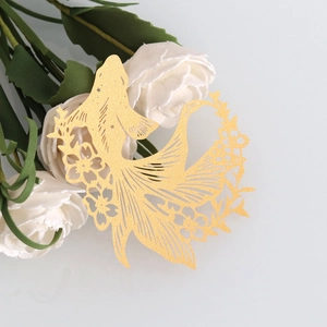 Detail of laser-cut gold fish wine glass card with intricate floral patterns for party decor