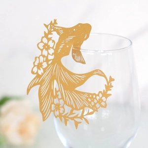 Detailed laser-cut golden koi fish paper decoration on a wine glass rim for parties