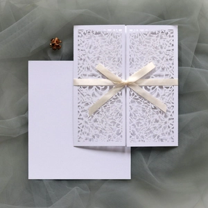 Detailed laser-cut vine patterns on white invitation card with elegant cream ribbon bow