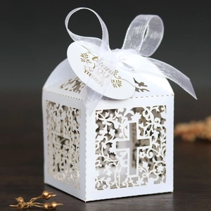 Detailed laser-cut white favor box with floral cross design, silk ribbon, and thank you tag