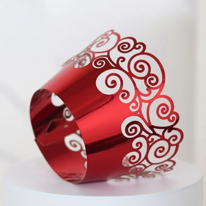 Macro shot of laser-cut red metallic cupcake wrappers with elegant scroll patterns