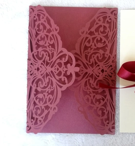 Detail of burgundy laser cut wedding invitation with intricate lace patterns and silk ribbon