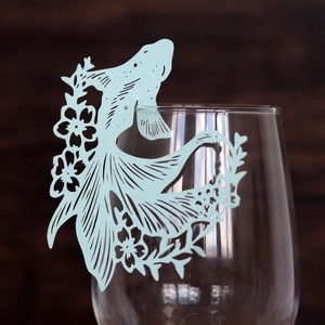 Close-up of laser-cut blue fish-shaped paper card decoration on a glass rim