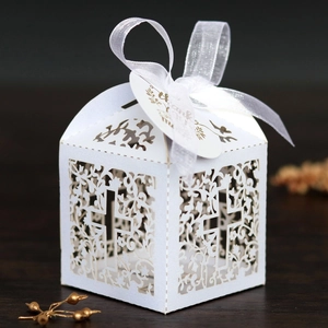 Close-up of laser-cut white wedding favor box with floral cross patterns and silk ribbon