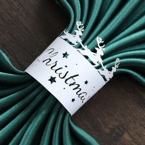Detail view of a white cutout reindeer Christmas napkin ring on dark green satin fabric