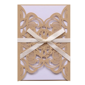 Detailed laser-cut scrollwork on kraft paper wedding invitation with cream satin ribbon