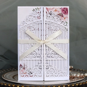 Detail of laser-cut white wedding invitation with beige ribbon and floral patterns