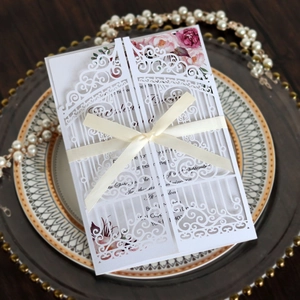 Detail of white laser-cut wedding invitation featuring elegant beige ribbon bow