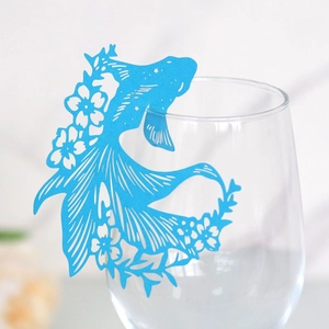 Macro view of blue laser-cut fish-shaped paper card decoration on a wine glass rim