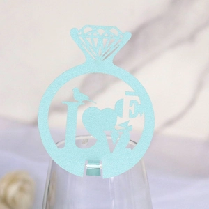 Detail view of light blue bird and LOVE hollow paper ring card on wine glass edge
